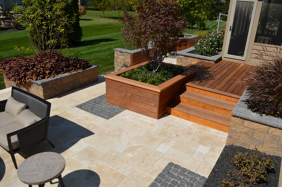 Travertine patio with a raised wood deck, built-in wood planters, and stone-capped seat walls beside a house