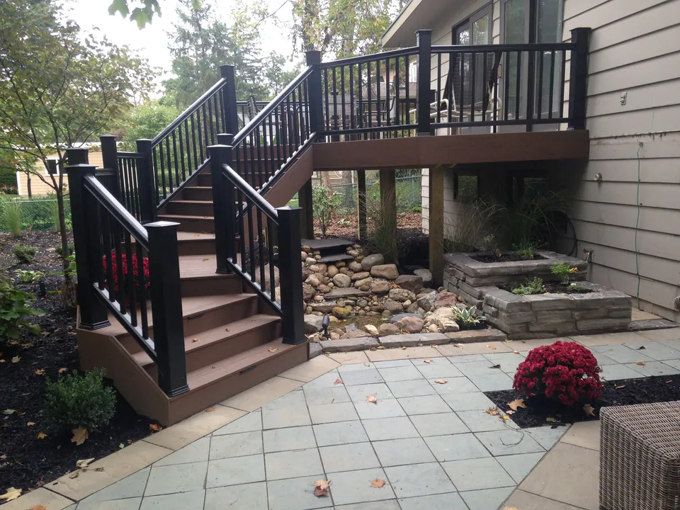 Raised deck with dark railings and a switchback stair down to a stone patio and garden
