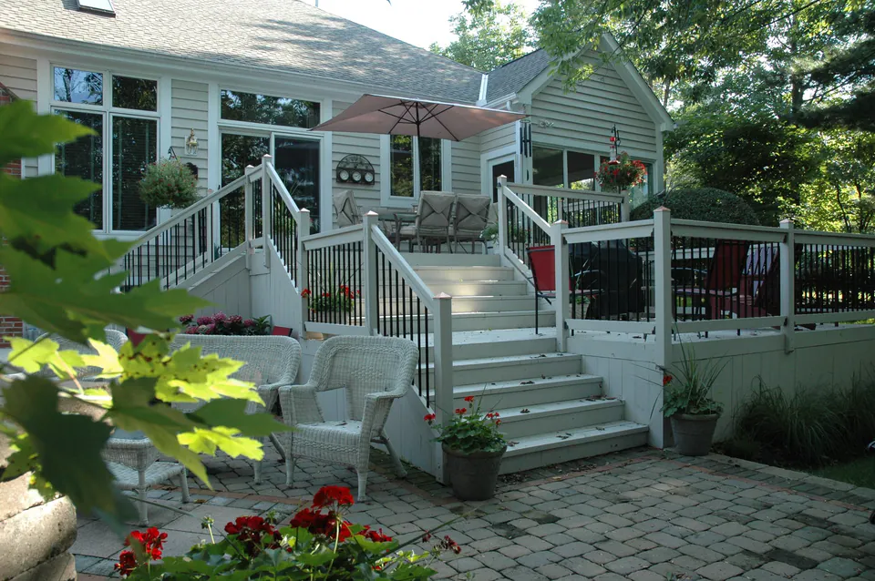 Deck with white railings and wide stairs stepping down to a paver patio with wicker seating