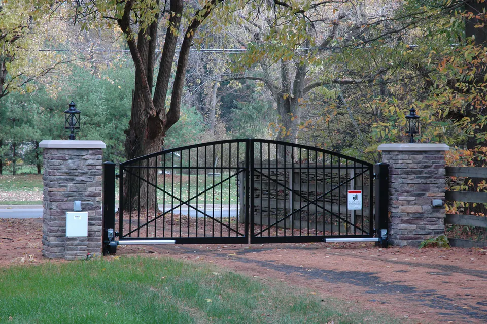 Arched black metal double gate between stacked stone piers with lanterns