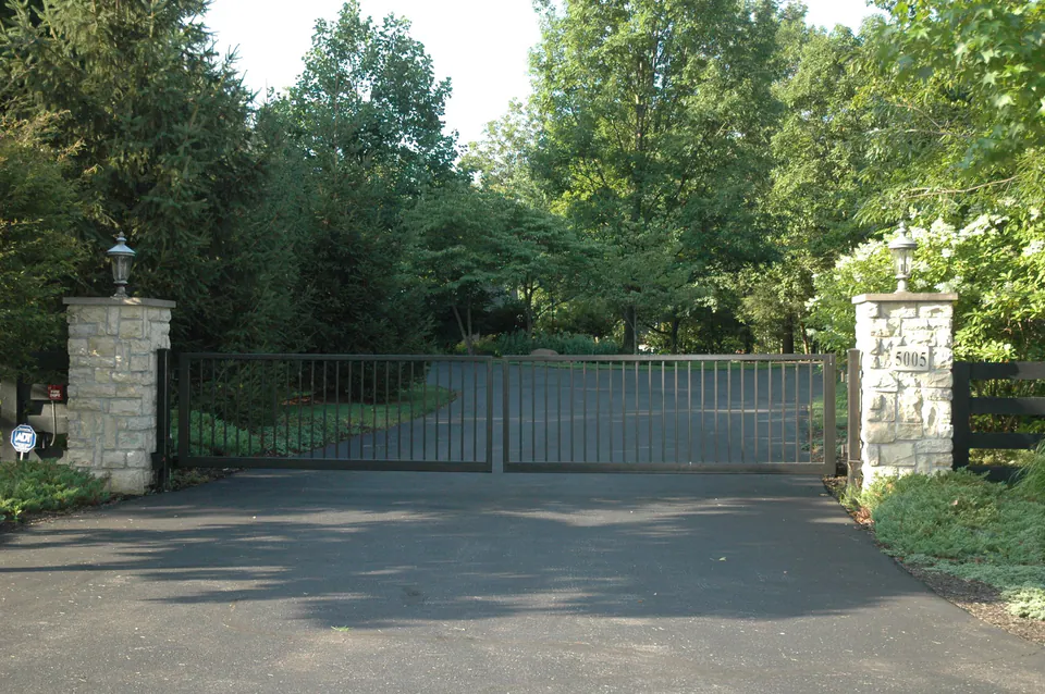 Black metal driveway gate between two cut stone piers with lanterns