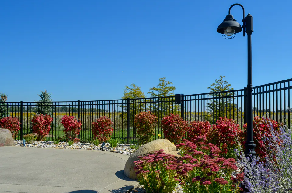 Black metal pool fence with perennial border, boulders, river rock, and black path light