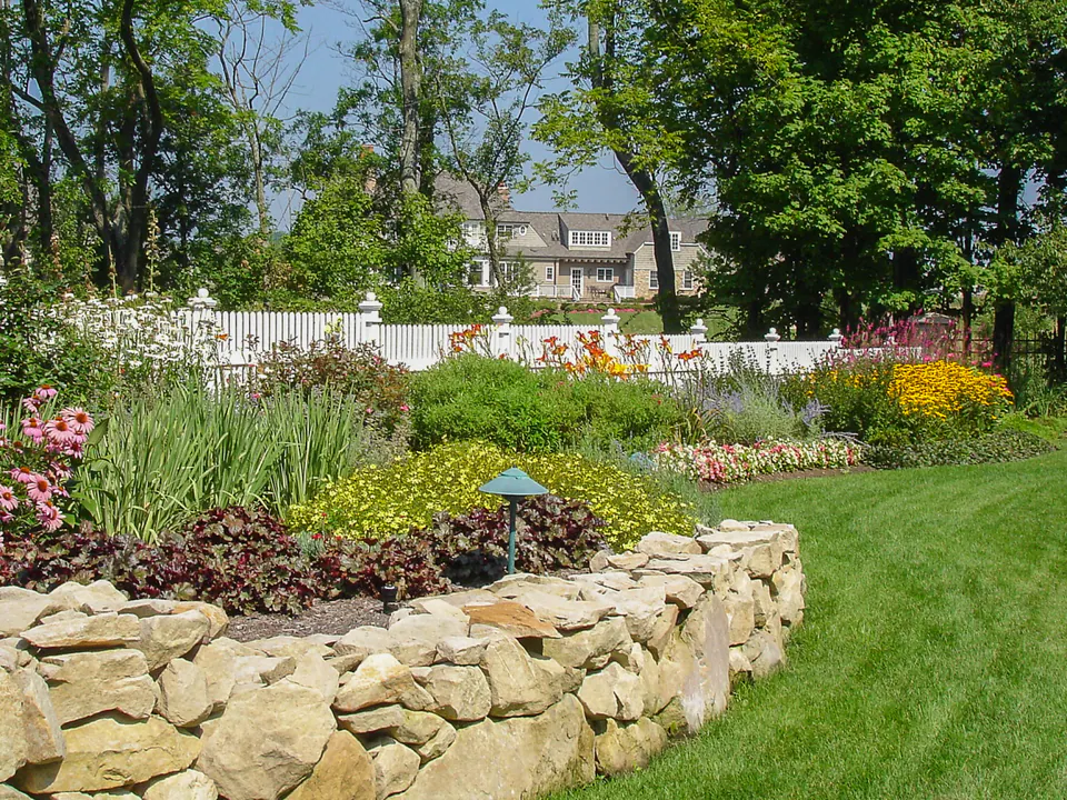 White picket fence behind a flowering garden bed and low stone wall