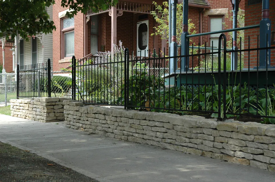Black metal fence set on a low dry-laid stone wall along a city sidewalk