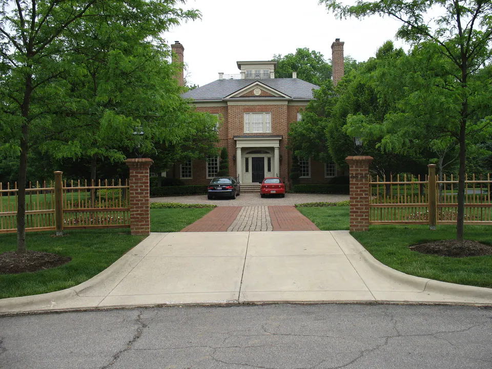 Stained wood picket fence with brick piers on each side of a brick-banded driveway