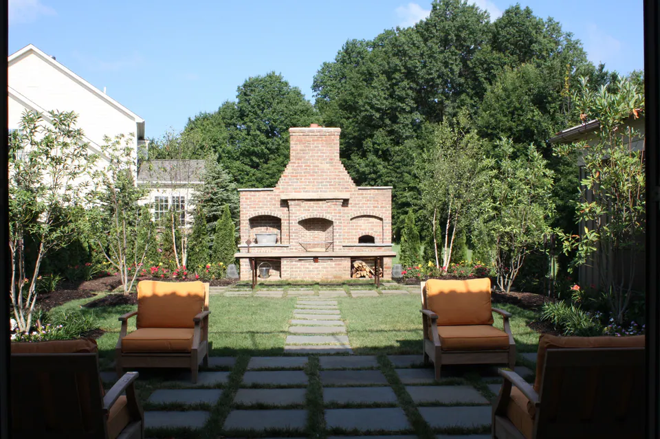 Brick outdoor fireplace with an oven at the far end of a lawn, with a stepping-stone path and chairs