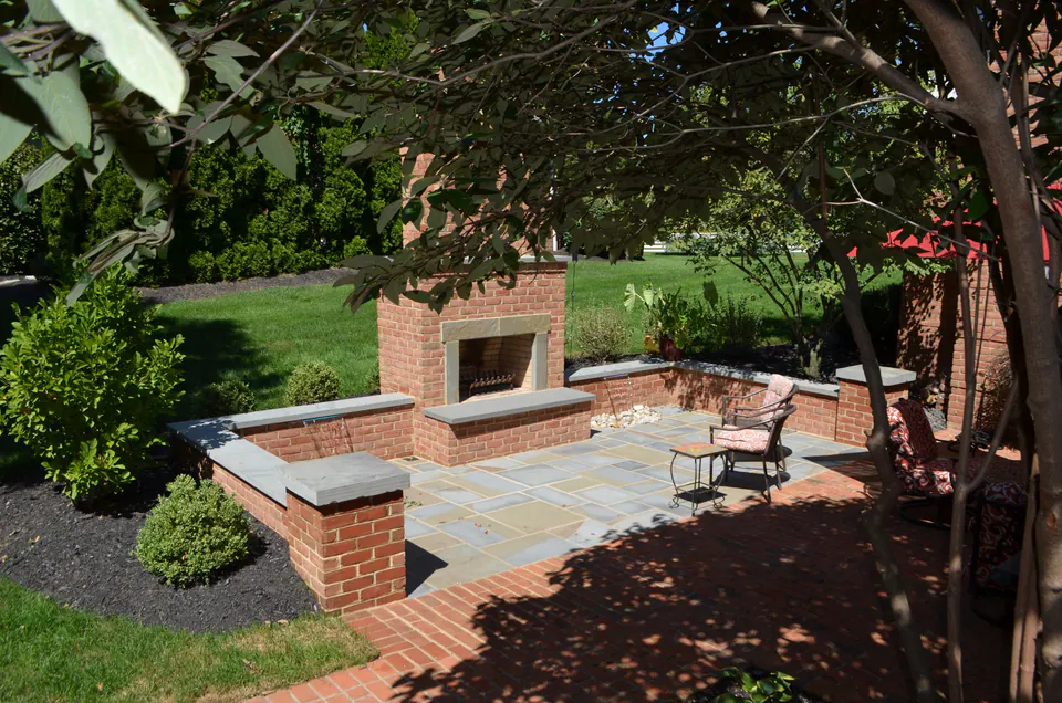 Brick outdoor fireplace at the end of a bluestone patio framed by low brick seat walls