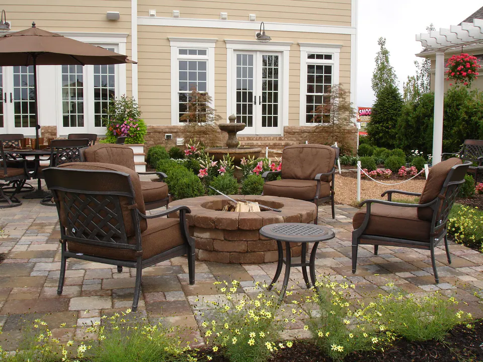 Round stone firepit on a paver patio surrounded by cushioned chairs and planting