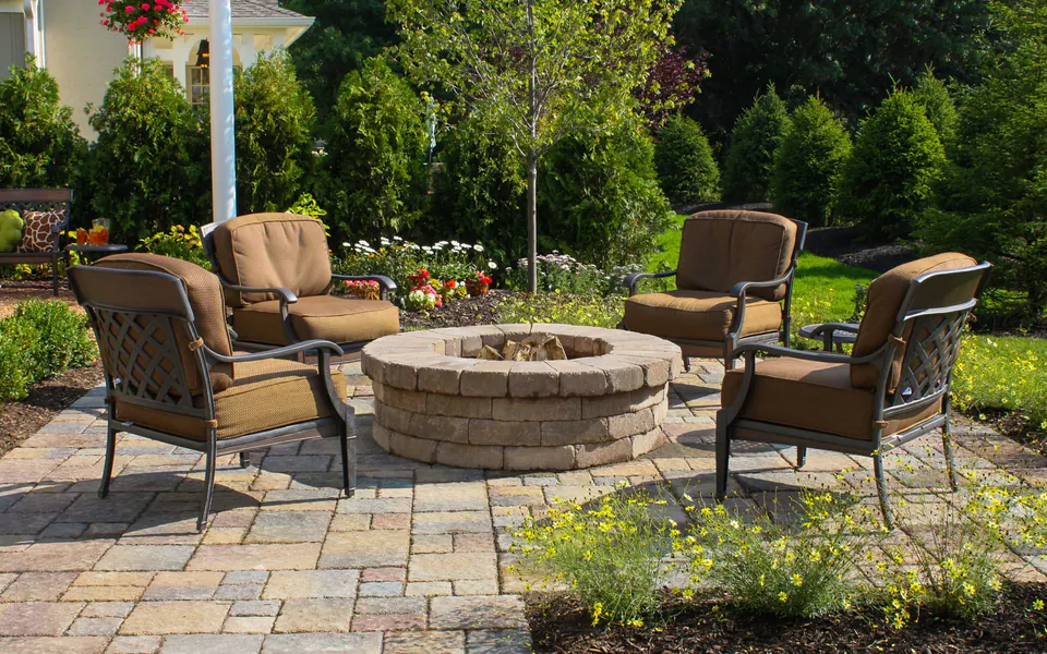 Round tumbled block firepit with cushioned chairs on a concrete paver patio with layered garden planting
