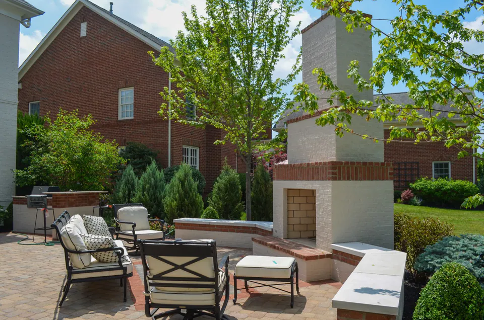 Painted brick outdoor fireplace with brick soldier course, cut stone caps, paver patio, grill station, and evergreen planting