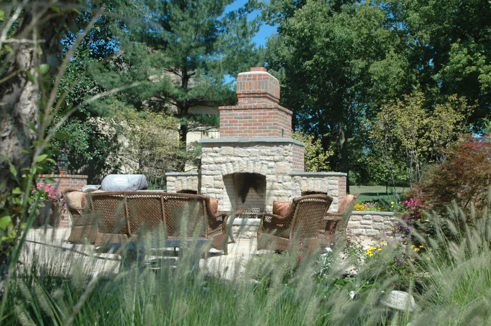 Outdoor stone fireplace with a brick chimney and wicker seating beside ornamental grasses