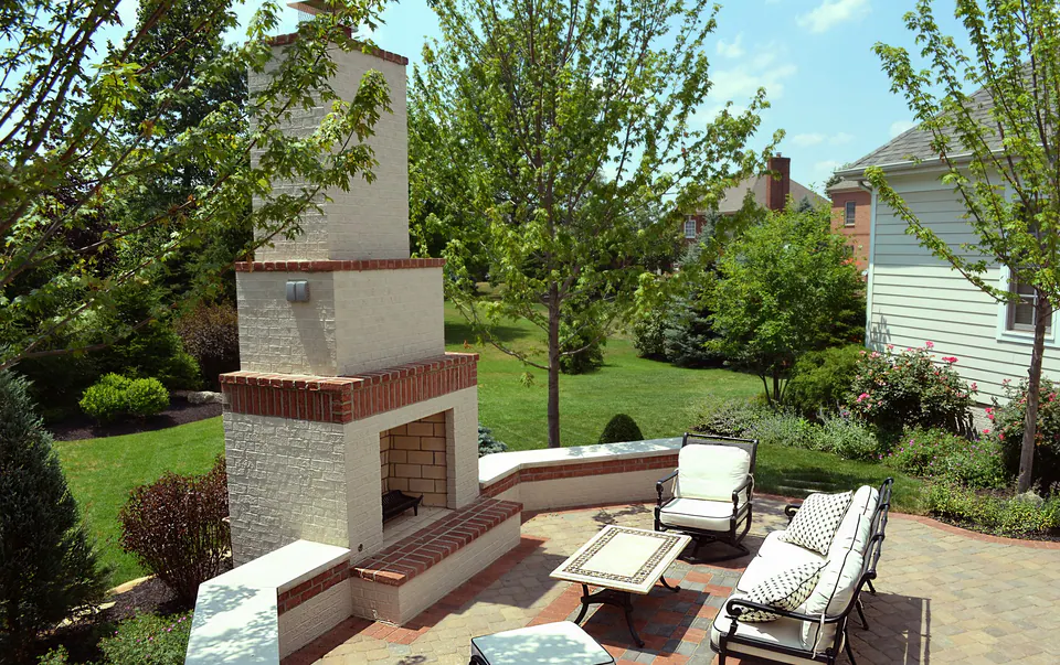 White painted brick fireplace with brick trim beside a paver patio and curved seat wall