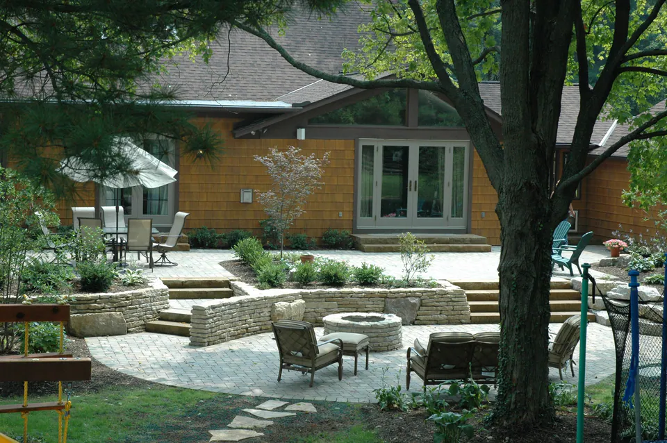 Round firepit in a lower patio ringed by stone seat walls and steps below a house