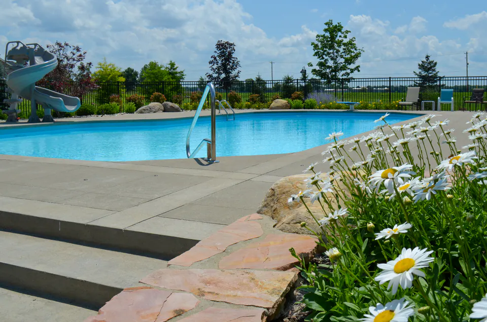 Pool deck with broad concrete steps, perennial flowers, pool railing, and lounge seating