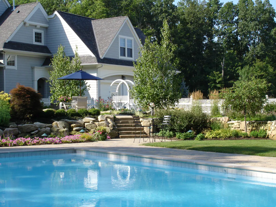 In-ground pool with a stone-terraced garden, steps and flowering beds rising to the house