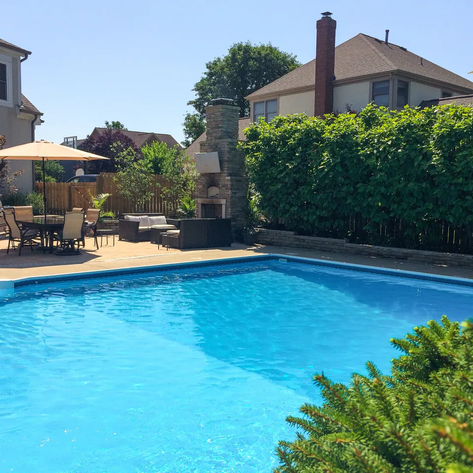 Swimming pool with privacy hedge, outdoor fireplace, dining area, wood fence, and seating at the pool edge