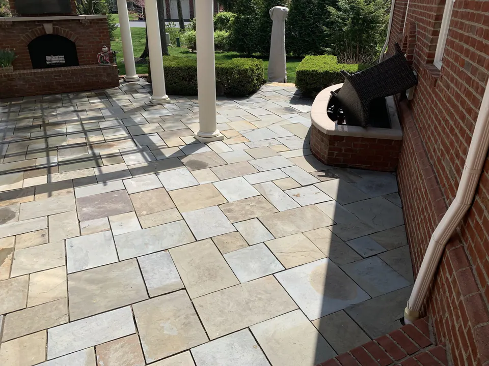 Pattern-cut bluestone patio with white columns and a brick fireplace beside a brick house