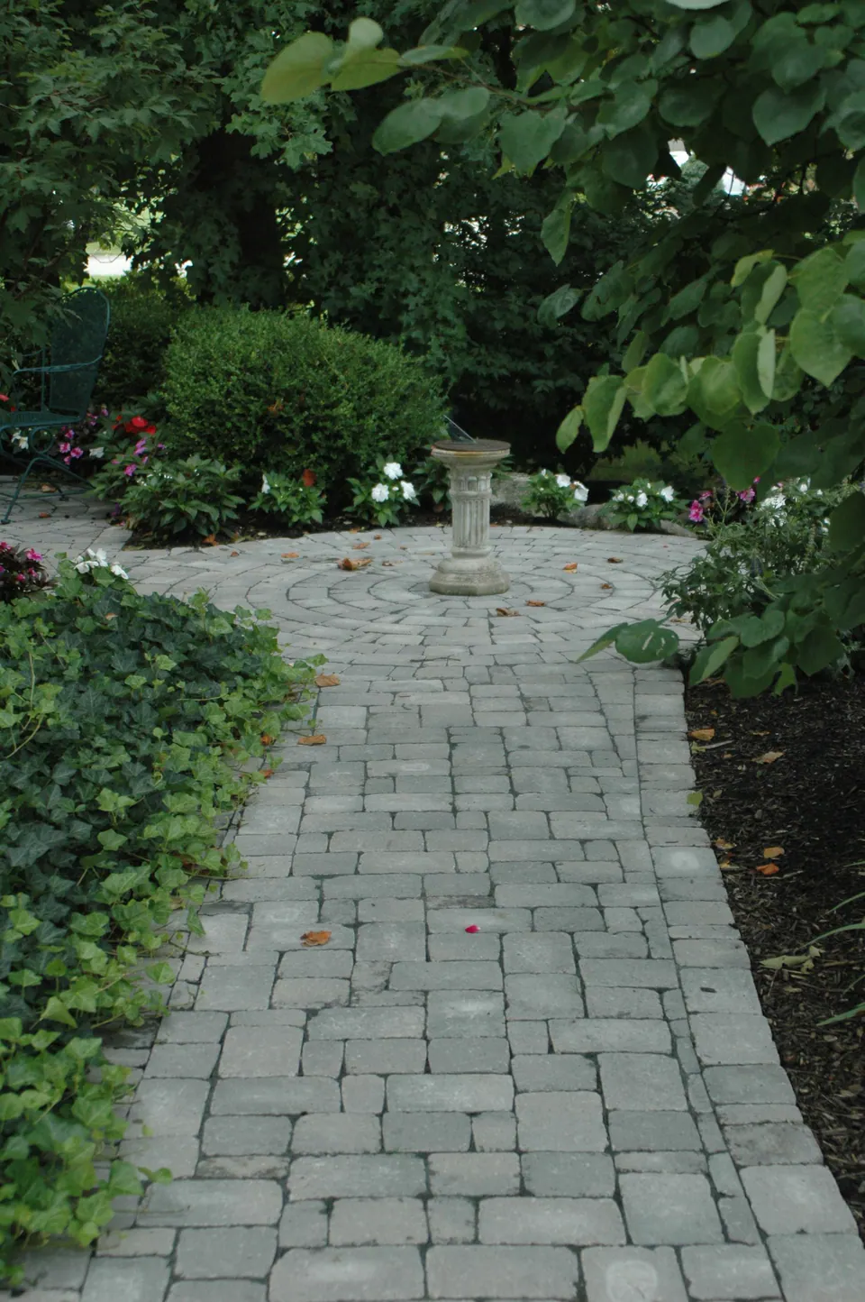 Tumbled paver walk leading through shade planting to a circle with a birdbath