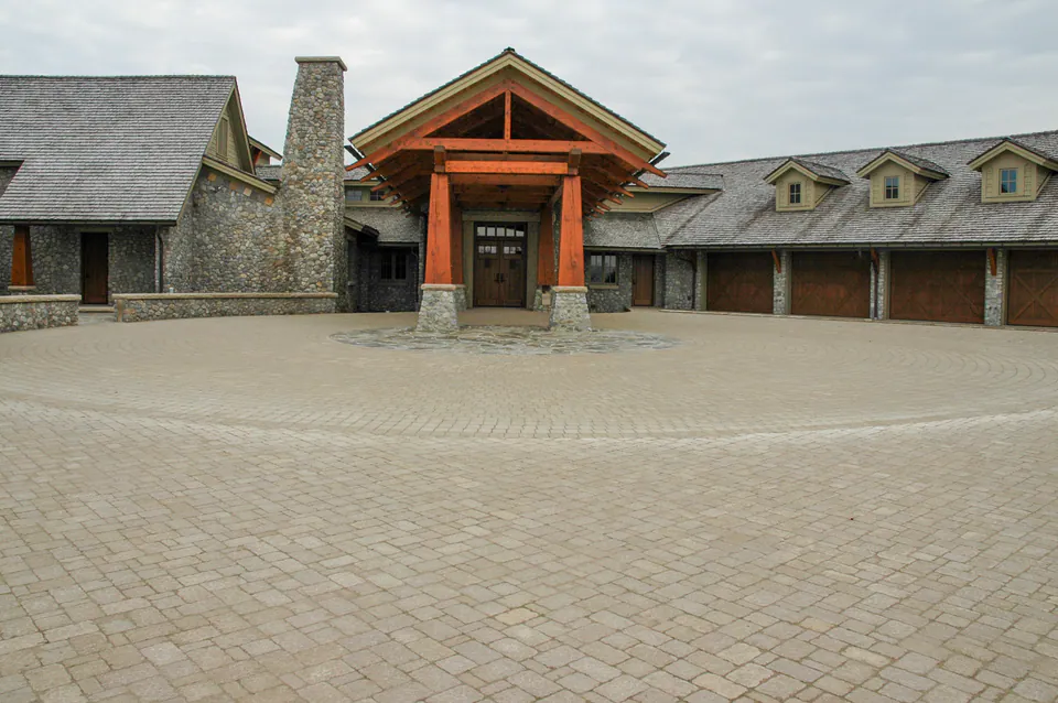Large paver driveway court in front of stone garage bays with a timber entry canopy and stone columns