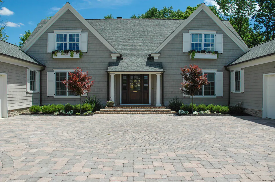 Paver motor court in front of a house with front entry, lawn, foundation planting, and garage wings