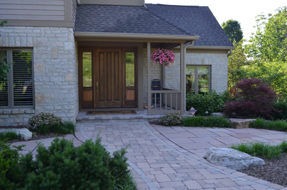 Paver front walk curving to a stone house entry with boulders and shrub beds