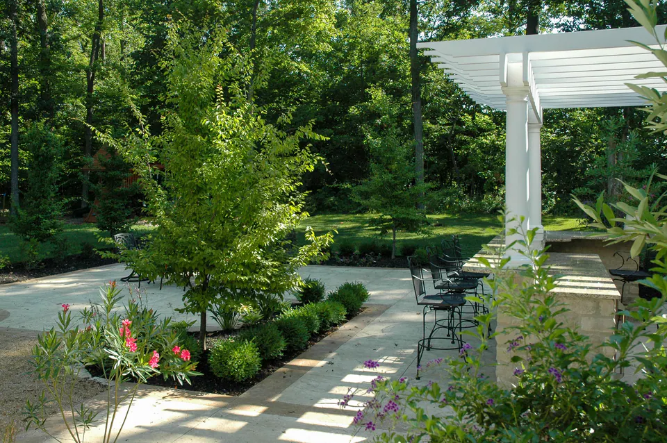 Pale natural stone patio beside a white pergola, limestone columns, boulders, and layered planting