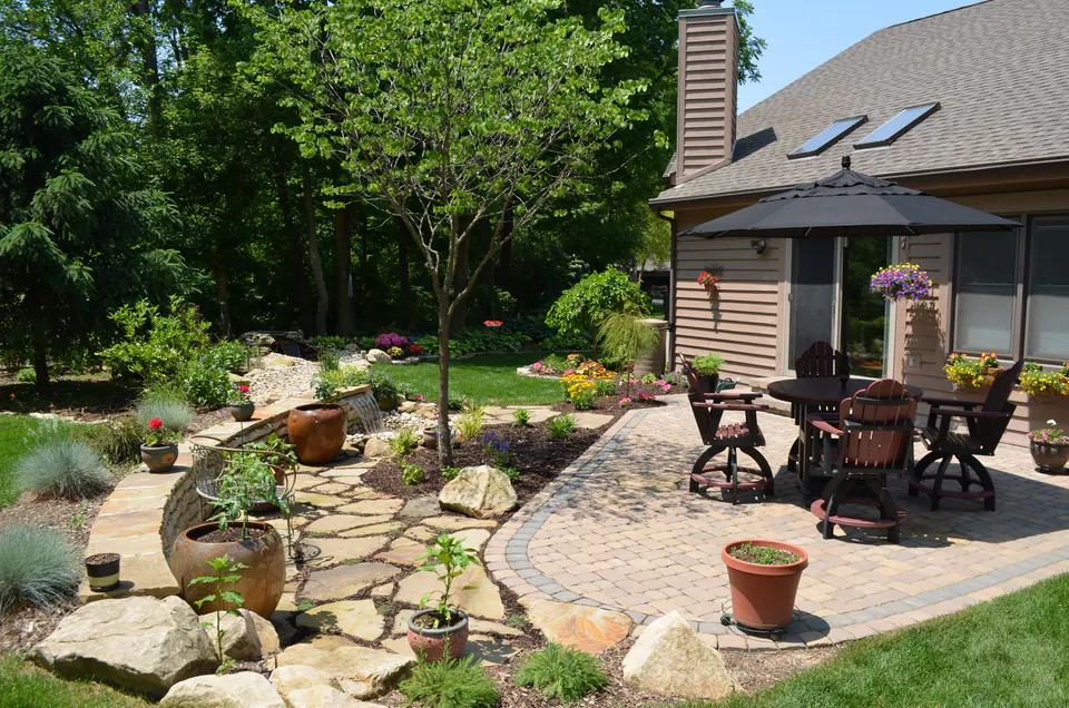 Paver dining patio beside a flagstone garden area with boulders, pots and a small tree