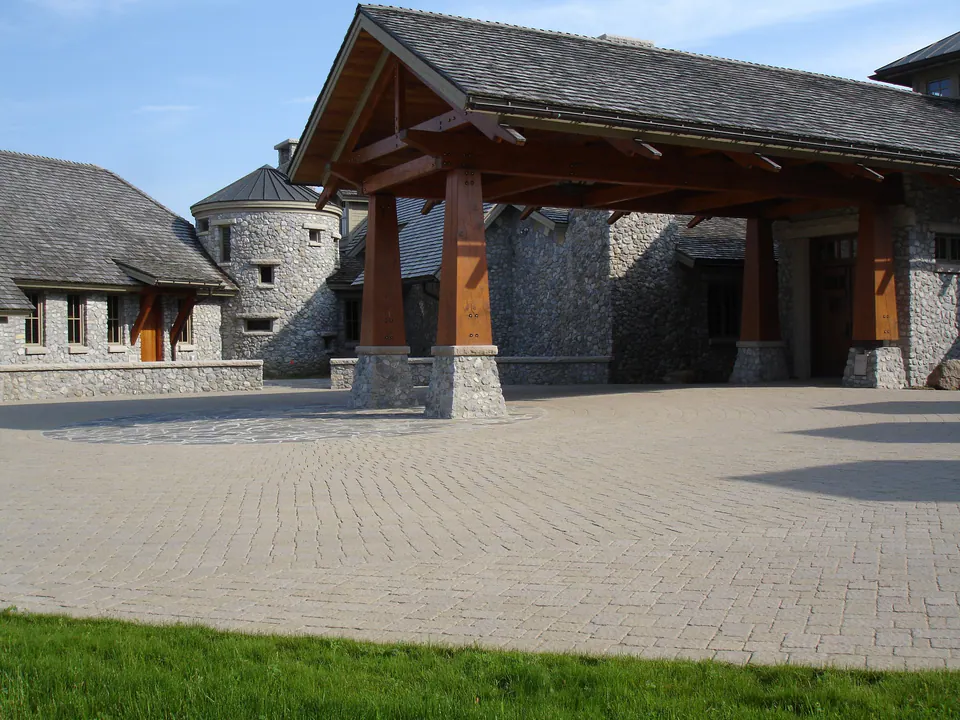 Large paver motor court in front of a stone house with a timber porte-cochere