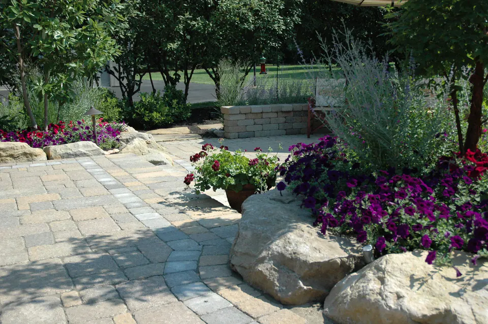 Paver patio edged with boulders, purple petunias and perennials beside a seat wall
