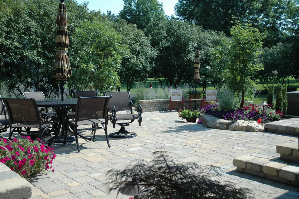 Paver patio with a dining table, umbrella, steps and planting beds with petunias