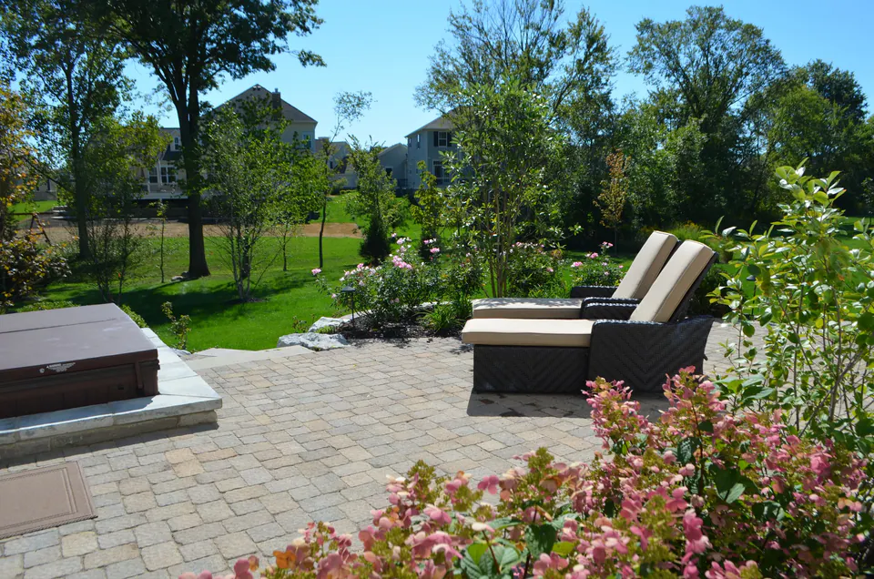 Paver patio with lounge chairs, flowering hydrangeas and a view to the lawn and trees