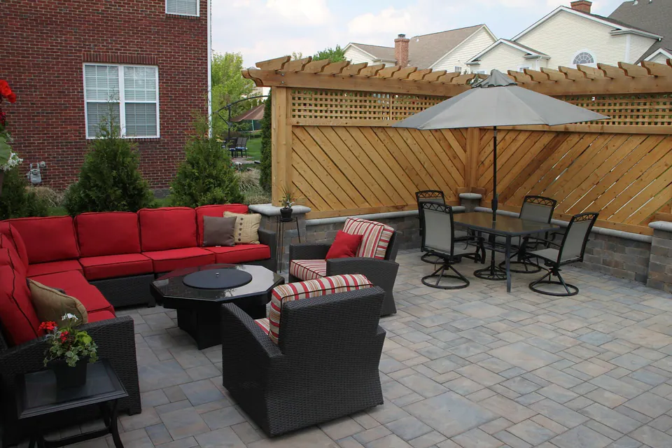 Paver patio with a red sectional, fire table and dining set in front of a cedar lattice privacy screen