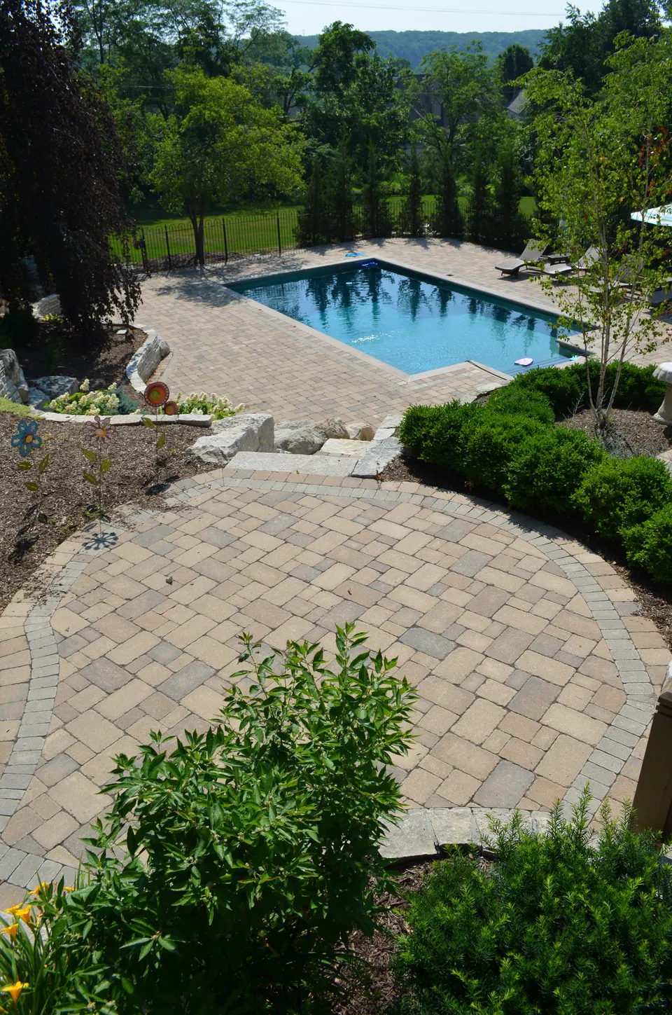Paver walk seen from above curving down through shrubs to a pool and deck