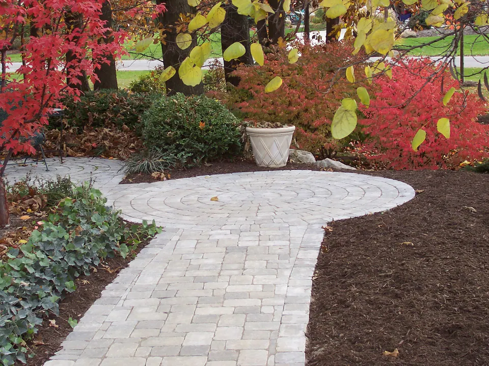 Paver walk leading to a round landing with a planter, surrounded by red and yellow fall color