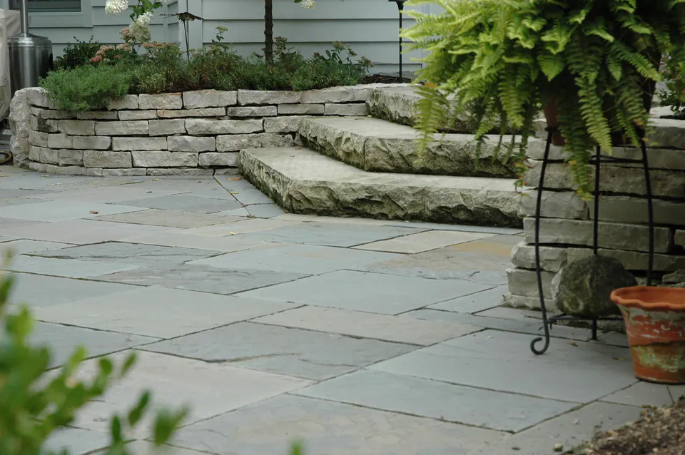 Bluestone patio with natural stone steps, limestone wall, hydrangea planting, hanging fern, and brick house