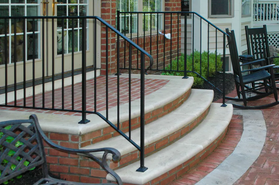 Curved brick entry steps with limestone treads, brick landing, and black metal handrails at a house entry