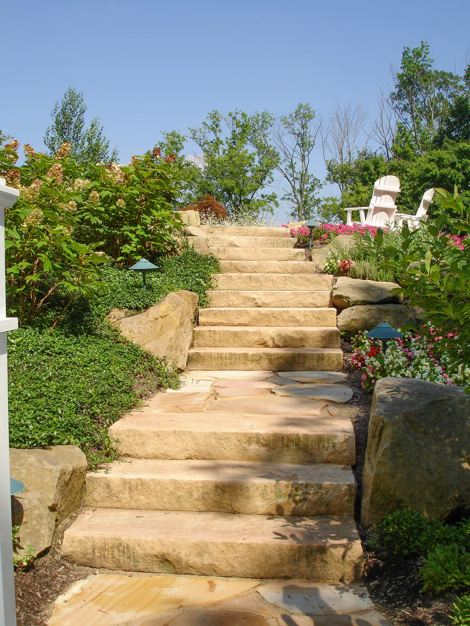 Long limestone outcropping stair climbing a planted hillside with boulders, flowering beds, and path lighting