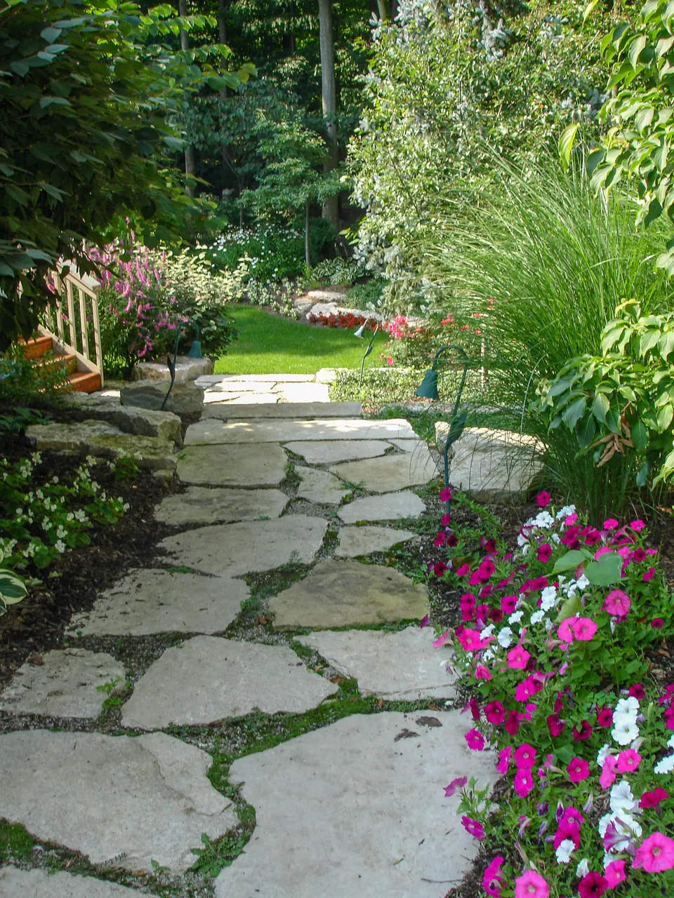 Irregular flagstone garden walk with planted joints, stone edging, annual flowers, ornamental grasses, and path lighting