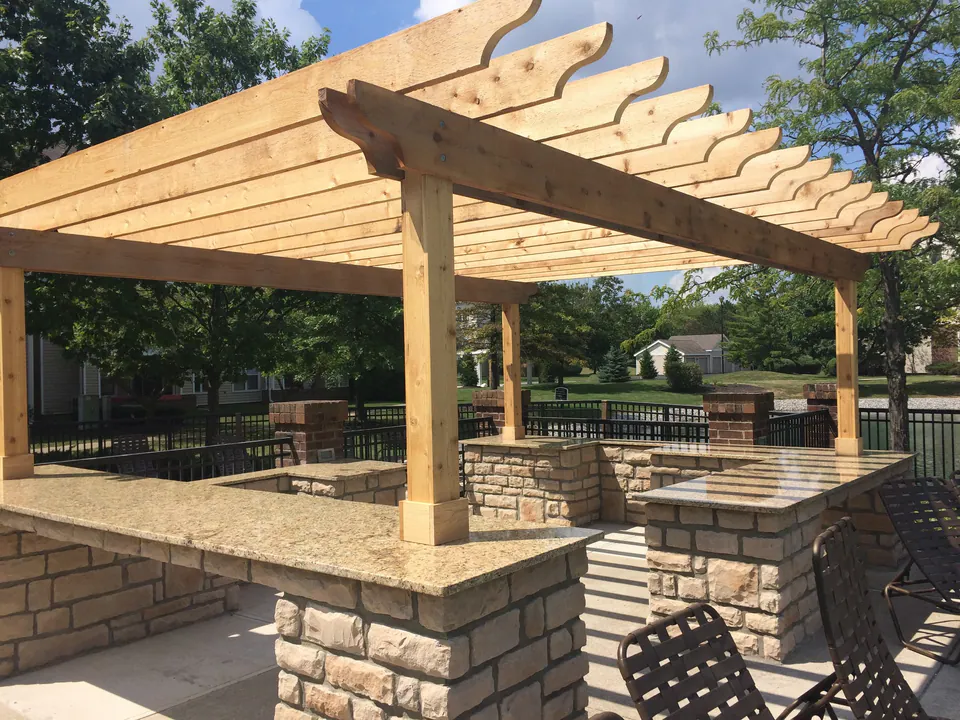 Cedar pergola over a stone bar counter with granite top beside a community pool