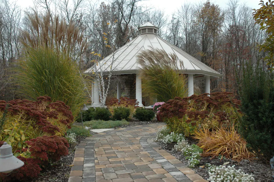 Octagonal garden pavilion with a cupola at the end of a curved paver walk lined with grasses
