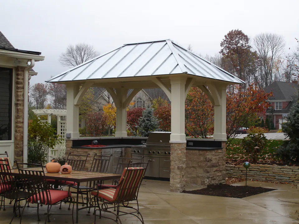 Open pavilion with a metal roof and white columns over a grill counter, with patio dining in front