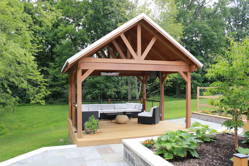 Timber pavilion with a metal roof over a wood lounge deck beside a bluestone patio and garden