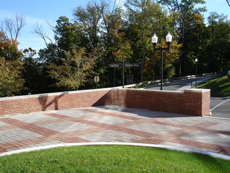 Brick seat wall and paver plaza with lamp posts and fall trees at a street corner