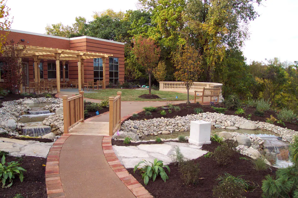 New landscape at a brick building with a stream, a wood footbridge, a paver walk, and fresh mulch beds