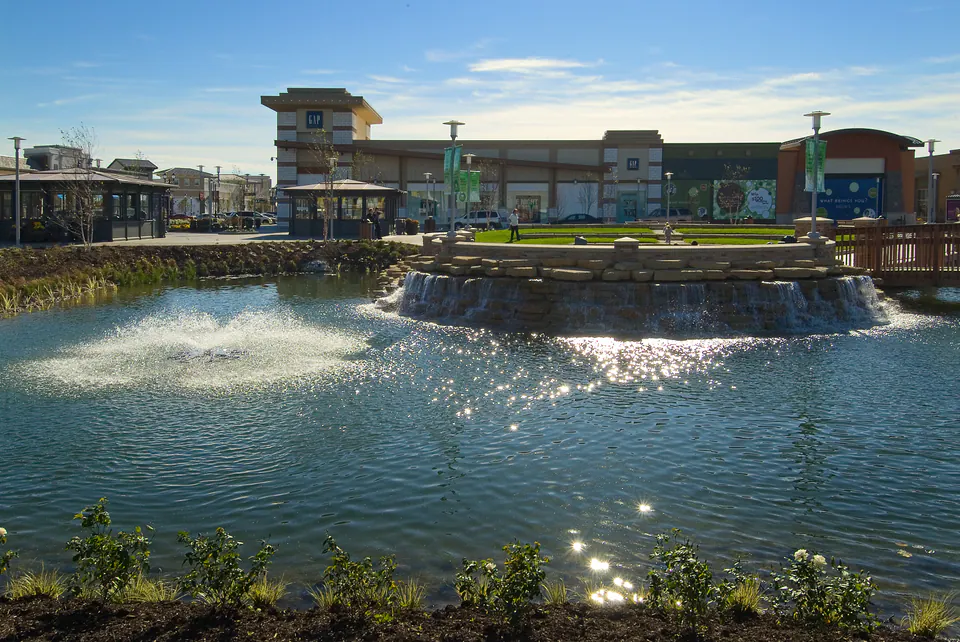 Stone waterfall wall spilling into a pond in front of a retail center under a blue sky