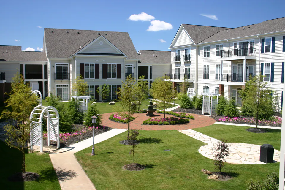 Apartment courtyard with a circular bed of annuals, a white arbor, young trees, and curved walks
