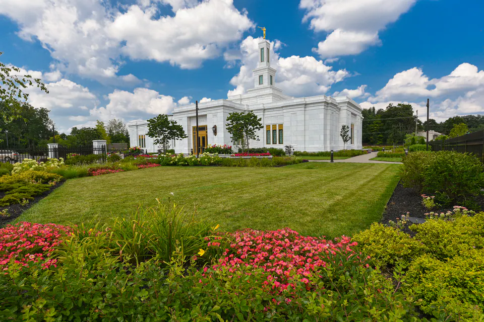 White temple building behind a formal lawn and beds of pink annuals under a blue sky