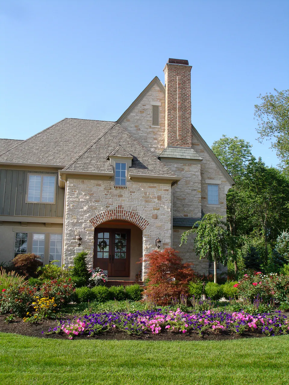 Stone and stucco house with a front entry bed of annual color, shrubs and a small ornamental tree