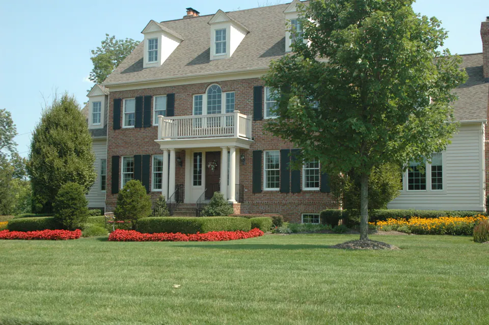 Colonial brick house with a broad lawn, red and yellow annual beds, and a mature shade tree