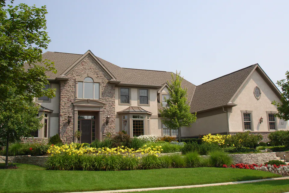 Stone and stucco house with yellow daylilies, ornamental grasses, and layered shrubs along the front